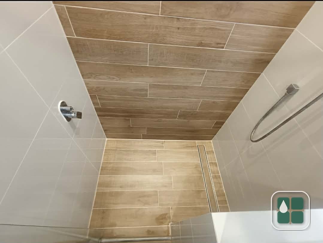 Shower recess lined with timber-look floor and wall tiles, with a linear strip drain along the edge and clean grout lines throughout.